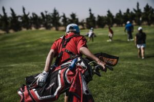 man walking carrying black and red golf bag on green grass field